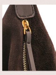 Close-up of a dark brown suede or faux-suede bag with a gold-tone zipper and a dark brown leather pull tab